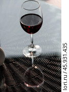 A glass of red alcoholic drink or wine on a glass table on the veranda. The concept of alcoholism, a party, or a holiday. Стоковое фото, фотограф Photojuli / Фотобанк Лори