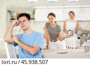 Disheartened young man sitting in kitchen with dissatisfied wife and mother-in-law. Стоковое фото, фотограф Яков Филимонов / Фотобанк Лори
