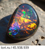 A close-up of an opal, a gemstone with a unique play of color. The oval-shaped stone is polished to a shine, with a deep black base and vibrant highlights that range from fiery orange and rich yellow to blue and green. Reflections and refractions create the illusion of cracks or fine lines within, reminiscent of branching patterns. The stone rests on a rocky surface that contrasts with its vibrant colors. The lighting highlights the opal's structure and shine, highlighting its natural beauty and complexity. Стоковое AI-изображение, AI-художник Анна Кривицкая / Фотобанк Лори