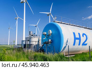 Hydrogen storage tanks marked with H2 and wind turbines stand in a green, eco-friendly landscape, under a bright sky. Стоковое AI-изображение, AI-художник Михаил Строгалев / Фотобанк Лори