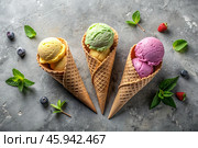 Sweet dessert. Ice cream cones with different flavors on a concrete gray background. World Ice Cream Day. Стоковое AI-изображение, AI-художник Photojuli / Фотобанк Лори