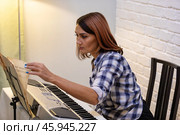 Beautiful woman in checkered shirt playing music synthesizer at home, composes music, learns musical scores. Стоковое фото, фотограф Ольга Яковенко / Фотобанк Лори
