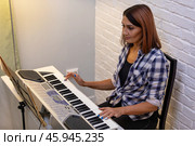Beautiful woman in checkered shirt playing music synthesizer at home, composes music, learns musical scores. Стоковое фото, фотограф Ольга Яковенко / Фотобанк Лори