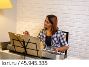 Beautiful woman in checkered shirt playing music synthesizer at home, composes music, learns musical scores. Стоковое фото, фотограф Ольга Яковенко / Фотобанк Лори