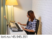 Beautiful woman in checkered shirt playing music synthesizer at home, composes music, learns musical scores. Стоковое фото, фотограф Ольга Яковенко / Фотобанк Лори