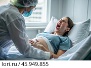 A pregnant woman in a hospital bed in the maternity ward. The woman is in labor and screaming in pain. Pregnancy and childbirth. Стоковое AI-изображение, AI-художник Photojuli / Фотобанк Лори