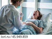 A pregnant woman in a hospital bed in the maternity ward. The woman is in labor and screaming in pain. Pregnancy and childbirth. Стоковое AI-изображение, AI-художник Photojuli / Фотобанк Лори