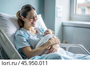 A woman in a hospital bed in the maternity ward. Mom has a newborn baby in her arms. Pregnancy and childbirth. Стоковое AI-изображение, AI-художник Photojuli / Фотобанк Лори