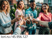 Glasses of pink sparkling wine in the hands of people. People are relaxing on the outdoor veranda. The concept of recreation, corporate event, party or celebration. Стоковое AI-изображение, AI-художник Photojuli / Фотобанк Лори