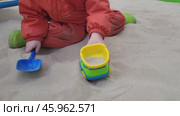 Kid in orange jumpsuit and green boots playing with plastic shovel, bucket, and toy excavator in sandbox. Outdoor play and early childhood activity. Стоковое видео, видеограф Андрей Журавлев / Фотобанк Лори