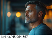 A middle-aged or older man with a noble appearance and an expressive profile. His face demonstrates confidence and maturity. Short hair with silver strands emphasizes his age, and a neat gray beard and stubble add charisma. The man is dressed in a simple blue T-shirt, which emphasizes his athletic or fit figure.The background of the image is blurred, using bokeh - large bright spots of light, reminiscent of lamps or evening lighting. Blue and warm orange shades of the background create a soft contrast and an atmosphere of thoughtfulness or peace. His gaze is directed into the distance, which can symbolize reflection, dreams or determination. Стоковое AI-изображение, AI-художник Анна Кривицкая / Фотобанк Лори