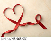 Heart shape and awareness ribbon created with red ribbon on a light marble surface conveying love and support. Стоковое AI-изображение, AI-художник Анна Сивакова / Фотобанк Лори