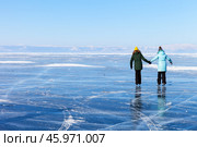 Two girls tourists skate on the blue ice of the frozen Lake Baikal near Cape Khoboy on a cold sunny February day. Beautiful winter landscape. Winter activity and outdoor recreations. Стоковое фото, фотограф Виктория Катьянова / Фотобанк Лори