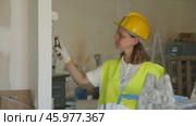 Professional female painter in protective helmet and yellow vest paints the walls with a paint roller. Стоковое видео, видеограф Яков Филимонов / Фотобанк Лори