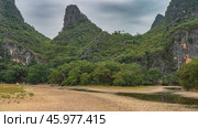 The picturesque mountains are covered with lush green vegetation. Peaks against the sky and clouds. Cows graze in the meadow. Puddles of water on the pebbly riverbank. China. Li River. LiJiang. Guilin. Стоковое фото, фотограф Вера Ивановна Кубарева / Фотобанк Лори