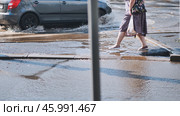 Commuter walking through large puddle on pedestrian crossing after heavy rainfall, with car splashing water nearby. Стоковое фото, фотограф Mikhail Davidovich / Фотобанк Лори