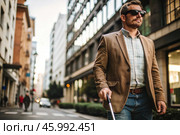 Disability. Loss of vision. A blind man with a cane and dark glasses is walking along a city street. International Day of the Blind on November 13. Стоковое AI-изображение, AI-художник Photojuli / Фотобанк Лори