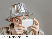 Man wearing tinfoil hat holding tablet with surprised expression. Стоковое AI-изображение, AI-художник Zakharova Natasha / Фотобанк Лори