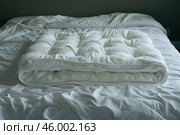 Folded white mattress pad on unmade bed. Стоковое AI-изображение, AI-художник Иван Рябоконь / Фотобанк Лори
