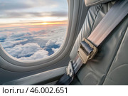 Airplane seat belt fastened with beautiful sunset view from window. Стоковое AI-изображение, AI-художник Иван Рябоконь / Фотобанк Лори