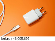 Белый блок питания и кабель USB на оранжевом фоне. Адаптер питания, зарядное устройство для бытовой электроники. Редакционное фото, фотограф Sergei Gorin / Фотобанк Лори