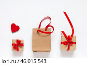 Valentine's Day gifts in eco-friendly paper boxes end bag with red satin ribbons and wooden red heart symbol of Valentine Day on white background. Copy space, flat lay, close-up, top view, mock up. Стоковое фото, фотограф Виктория Катьянова / Фотобанк Лори
