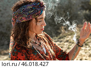 Женщина с этническим узором на лице, красиво освещённым солнцем, вдыхает дым от горящих благовоний. Стоковое фото, фотограф Elena Kotova / Фотобанк Лори