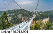 The longest glass suspension bridge in the world. People walk over a precipice on a transparent surface. Stretched support cables against the sky and rocks. China. Zhangjiajie Glass Bridge. Стоковое фото, фотограф Вера Ивановна Кубарева / Фотобанк Лори