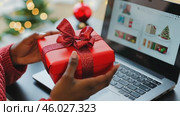 Online shopping at Christmas holidays. Woman buying Xmas gifts online with laptop, sitting next to decorated tree. Female hands hold a cozy red wrapped present among vibrant festive decorations. Стоковое AI-видео, аниматор Марина Демидюк / Фотобанк Лори