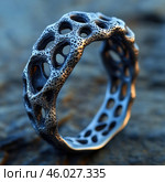 A metal ring with an unusual texture and design. It is made in the style of organics or biomorphism, with an uneven surface and many holes reminiscent of corals or a porous structure. Light falls on the ring, emphasizing its complex shapes and metallic shine. The background is blurred, which focuses attention on the object. The ring looks like a piece of modern jewelry art, combining nature and technology. Стоковое AI-изображение, AI-художник Анна Кривицкая / Фотобанк Лори