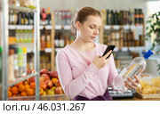 Female buyer checks suitability - scans QR code on bottle of water label in grocery store. Стоковое фото, фотограф Яков Филимонов / Фотобанк Лори