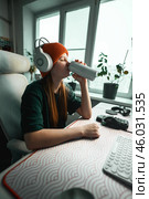 Focused gamer refreshes with an energy drink at her stylish desk. The scene captures creativity and motivation, blending modern technology and comfort in a productive daily routine. Стоковое фото, фотограф Енваев Андрей / Фотобанк Лори