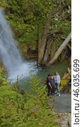 Vertical video: people taking pictures in a scenic location overlooking a breathtaking waterfall. Outdoor activities in the beautiful Caucasus mountains. Вертикальное видео: люди фотографируются в живописном месте с видом на захватывающий дух водопад. Активный отдых в живописных горах Кавказа. Редакционное видео, видеограф Валерий Тесаков / Фотобанк Лори