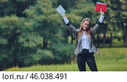 Student celebrating academic achievement, clutching textbooks overhead while standing in golden leafed autumn park. Стоковое фото, фотограф Mikhail Davidovich / Фотобанк Лори