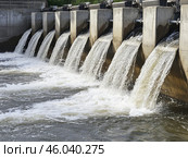 Dam with Waterfall on the River. Hydroelectric dam during Spring runoff, full water. Water rushing out of opened gates of hydro electric power dam. Concrete foothill and wall. Renewable energy systems. Стоковое AI-изображение, AI-художник Марина Демидюк / Фотобанк Лори