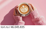 Coffee Cup. Female Hands in Wool Sweater Holding Cappuccino. Top view Woman with White Latte Mug. Close Up. Hygge Winter Mood. Cappuccino with Leaf Shape Art Milk Foam on Pale Pink Desk. Thick Froth. Стоковое AI-видео, аниматор Марина Демидюк / Фотобанк Лори
