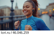 Девушка в синем спортивном костюме, в наушниках, бежит по мосту, ее лицо озаряет яркая улыбка. Стоковое фото, фотограф Ярославский Максим / Фотобанк Лори