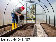A male farmer pours new soil, soil for a new greenhouse. The concept of spring vegetable planting, greenhouse installation and farming. Стоковое фото, фотограф Photojuli / Фотобанк Лори