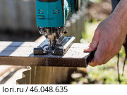 A man holds a battery-powered electric saw and builds new beds in a greenhouse made of wood-polymer composite. Macro photography. Side view. Preparing for the spring garden season. Стоковое фото, фотограф Photojuli / Фотобанк Лори