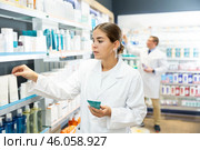 Young apothecary holding lubricant standing next to shelves with medical products. Стоковое фото, фотограф Яков Филимонов / Фотобанк Лори