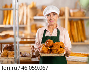 senior bakery worker sells croissants and shows off a variety of crescent-shaped buns. Стоковое фото, фотограф Яков Филимонов / Фотобанк Лори
