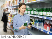 Positive woman reading label on bottle of Korean soju in Asian store. Стоковое фото, фотограф Яков Филимонов / Фотобанк Лори