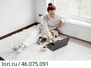 Smiling Young Woman Sitting on carpet and using Laptop by dog at Home. Стоковое фото, фотограф Гладских Татьяна / Фотобанк Лори