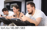 Focused bearded man works out with stationary bicycle during class at fitness club. Стоковое видео, видеограф Яков Филимонов / Фотобанк Лори