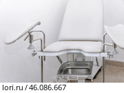 White modern gynecological examination chair for women. Medical chair in the gynecologist's office with white wall. Reproductive system and Pregnancy concept. High quality photo. Copy space. Стоковое фото, фотограф Ирина Михайличенко / Фотобанк Лори