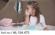 Fashion little girl in a white T-shirt is sitting at the dressing table in front of the mirror and applying makeup with eye shadow. Advertising of children's cosmetics concept. Footage for kids blog. Стоковое видео, видеограф Ирина Михайличенко / Фотобанк Лори