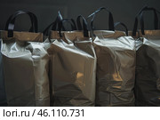 Many shiny shopping bags with black handles resting on dark surface. Стоковое AI-изображение, AI-художник Иван Рябоконь / Фотобанк Лори