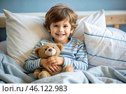 A cute boy hugs a teddy bear, sitting in a cozy bed, a small child hugs a toy and gets ready for bed. A healthy night's sleep. Стоковое AI-изображение, AI-художник Photojuli / Фотобанк Лори