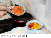 Женские руки высыпают морковь на сковороду с подогретым маслом, рядом стоят тарелки с подготовленными к жарке перцем и луком. Стоковое фото, фотограф Алиса Сокол / Фотобанк Лори