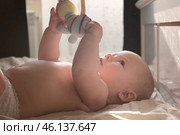 Cute Newborn Baby Lying on the Back and Plays with Colorful Toys. Little Three Month Child Takes a Toy. Playful Neonate Toddler. Concept of Childhood, New Life, Baby Care. Side view. Стоковое фото, фотограф Марина Демидюк / Фотобанк Лори